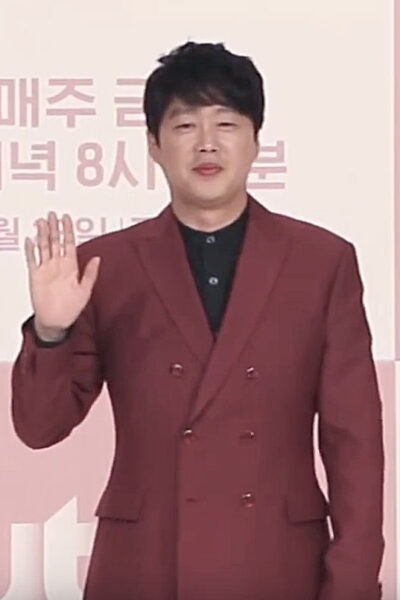 Kim Hie-won in a burgundy double-breasted suit and black shirt, waving at a JTBC drama press conference