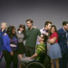 Glee cast key art: the ensemble of the Fox musical series posing together against a grey backdrop