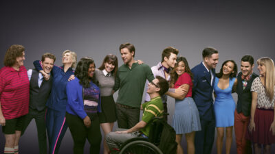 Glee cast key art: the ensemble of the Fox musical series posing together against a grey backdrop