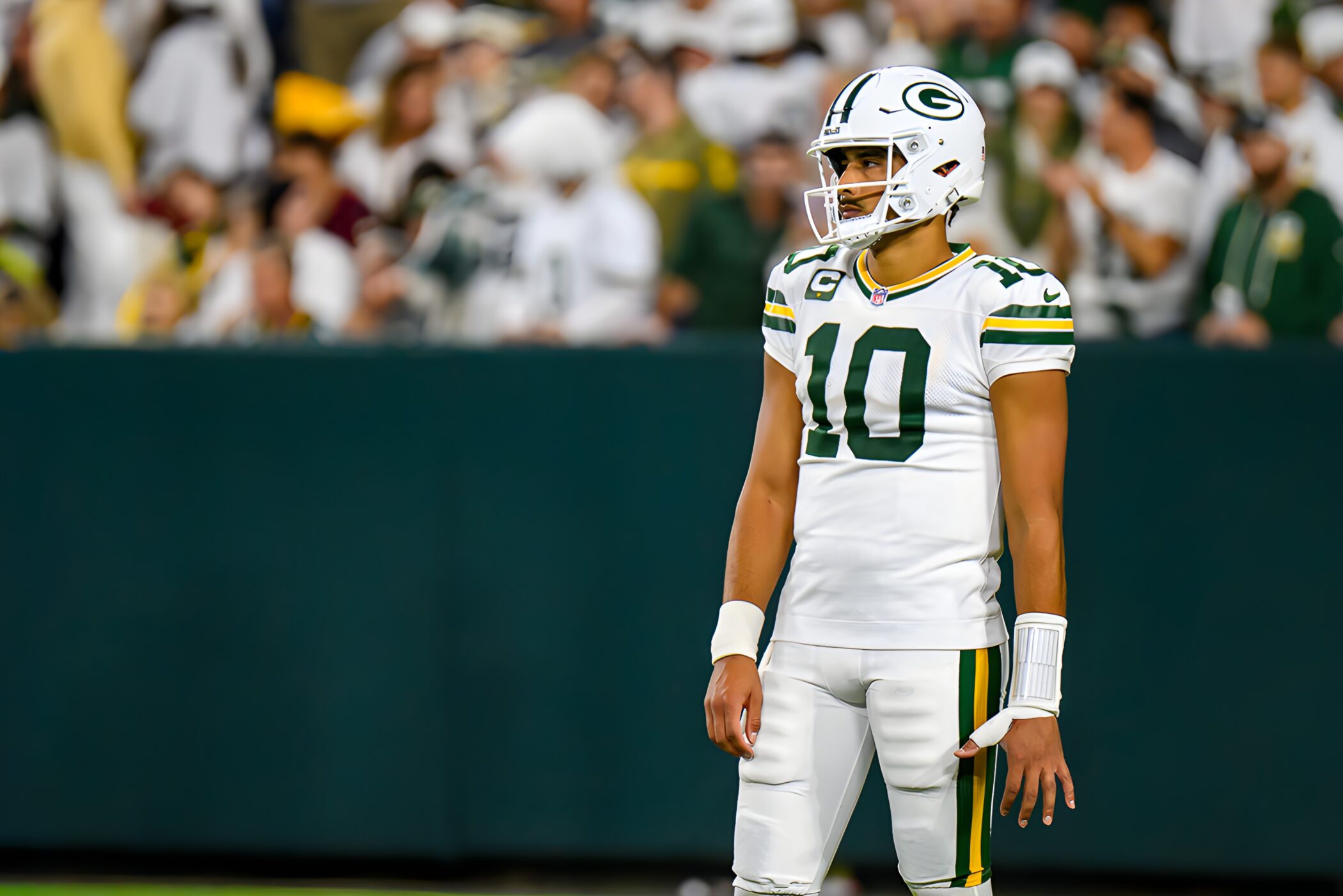 Jordan Love in the white Green Bay Packers No. 10 jersey with captain patch, standing on the field at Lambeau Field during a night game against Washington, 2025