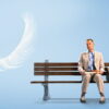 Tom Hanks as Forrest Gump sitting on a park bench with a suitcase and a box of chocolates, in the film’s key art