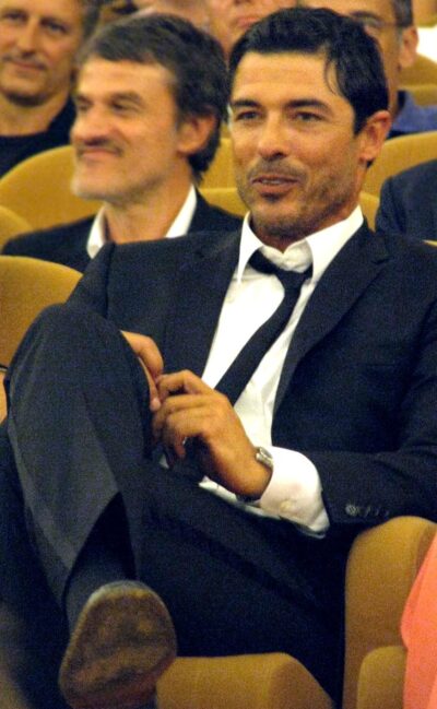 Alessandro Gassmann in a dark suit and loosened black tie, seated in a cinema audience at the 2008 Venice Film Festival
