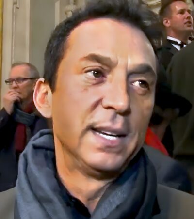 Bruno Tonioli in a grey scarf, speaking to camera at the opening night of Beautiful: The Carole King Musical, 2015