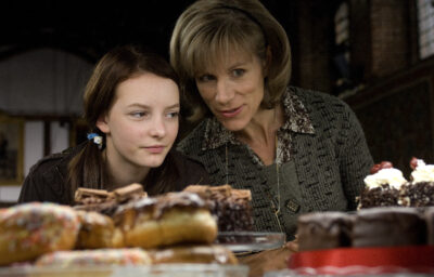 Juliet Stevenson leaning beside Dakota Blue Richards over a counter of cakes in a publicity still for the 2008 film Dustbin Baby