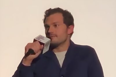 Jamie Dornan, in a navy cardigan, speaks into a microphone during a film Q&A