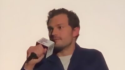 Jamie Dornan, in a navy cardigan, speaks into a microphone during a film Q&A
