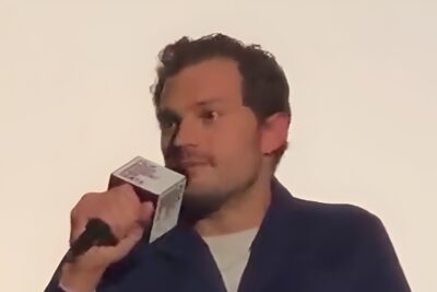 Jamie Dornan, in a navy cardigan, speaks into a microphone during a film Q&A