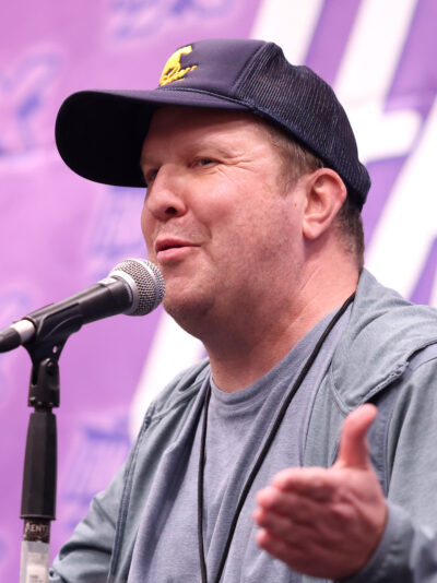 Nick Swardson in a navy trucker cap speaking into a microphone at a fan convention panel in Salt Lake City, 2026