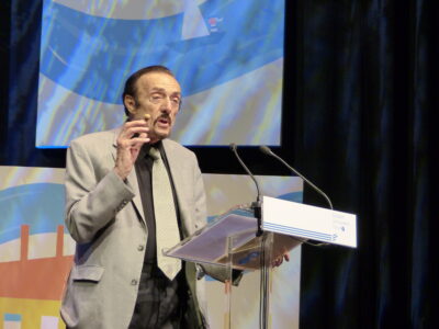 Philip Zimbardo speaking at a lectern in a grey jacket, Budapest, May 2017