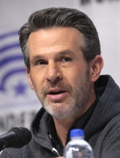 Simon Kinberg speaking into a microphone on a WonderCon panel in Anaheim in 2019, wearing a dark grey hoodie