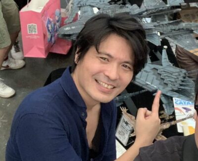 Hidetaka Tenjin smiling and pointing at Macross model kits on display at Wonder Festival Shanghai in 2018