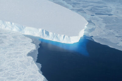Aerial view of the white ice cliff of Thwaites Glacier's ice shelf meeting dark blue open water in West Antarctica