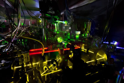 Laser beams in red, green, yellow and violet crossing the optics of the NIST ytterbium lattice atomic clock in a dark laboratory