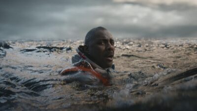 Idris Elba as astronaut Jackson surfacing in a rough grey ocean in Above the Below