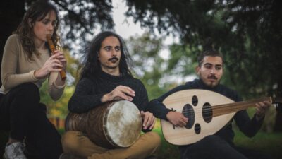Al Tayr Ensemble musicians playing a recorder, a goblet drum and an oud outdoors
