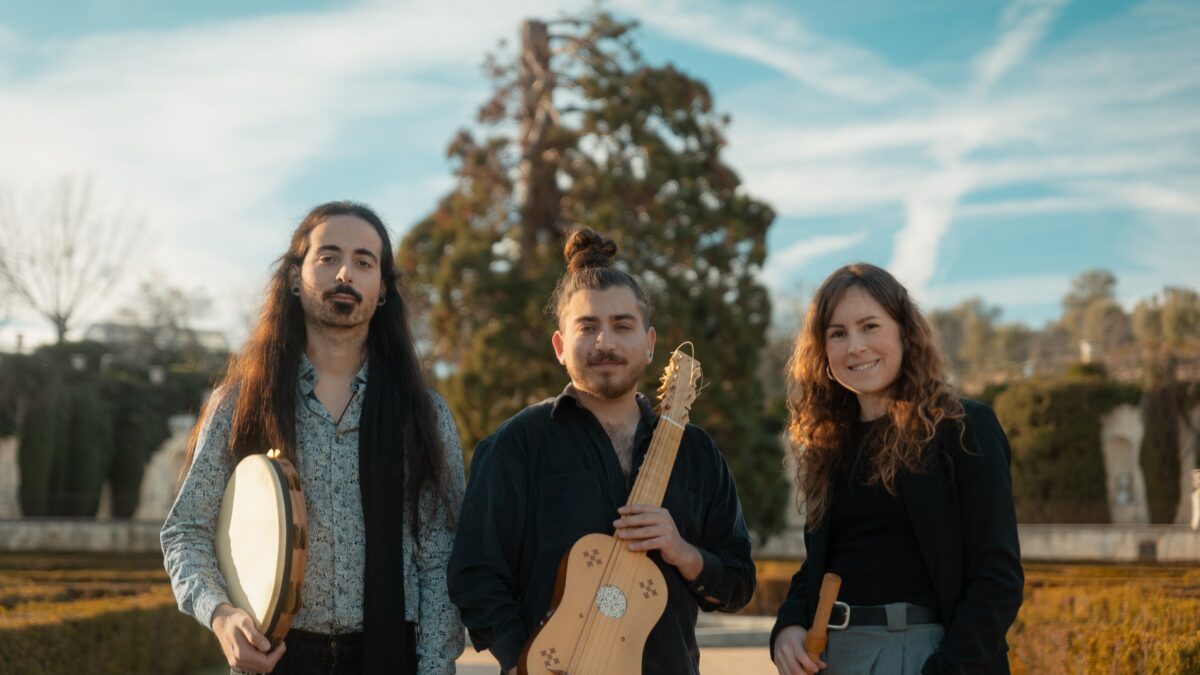 The three members of Al Tayr Ensemble holding a frame drum, a vihuela and a recorder in a garden