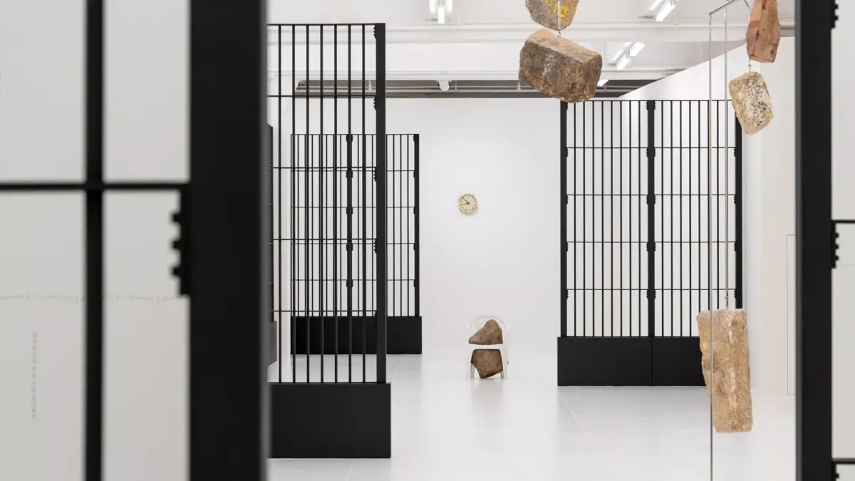 Suspended stones and black steel grilles in a white gallery, an Alicja Kwade installation