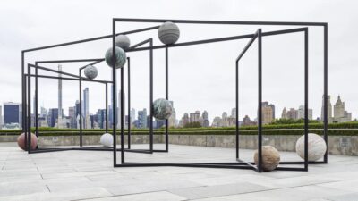 Black steel frames holding stone spheres on the roof of the Metropolitan Museum of Art, with the Manhattan skyline behind