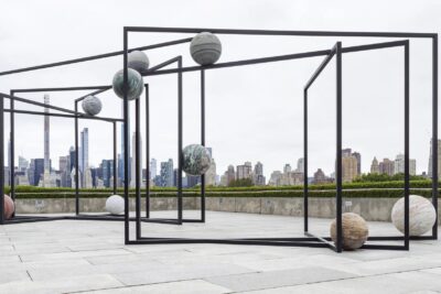 Black steel frames holding stone spheres on the roof of the Metropolitan Museum of Art, with the Manhattan skyline behind