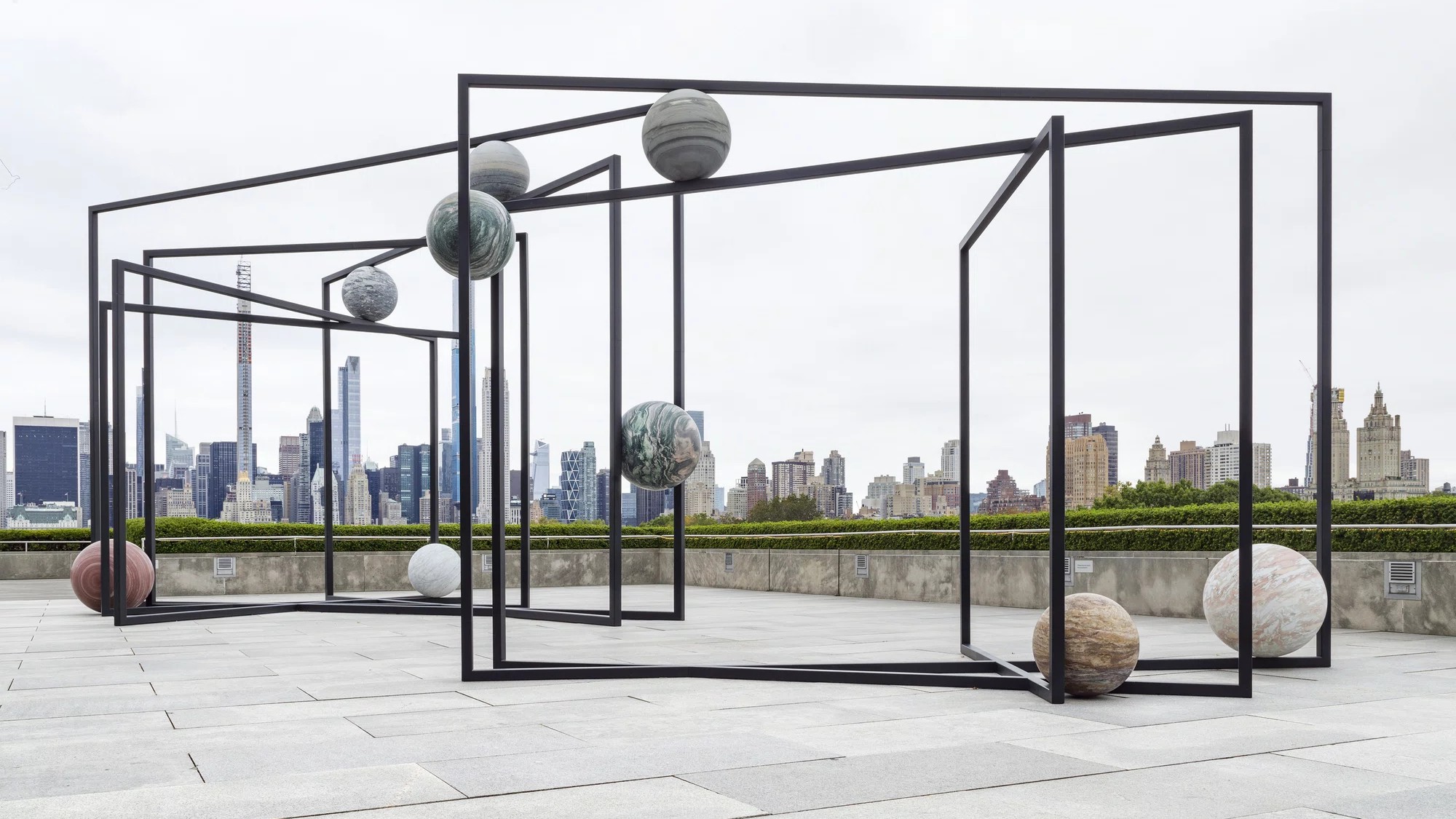 Black steel frames holding stone spheres on the roof of the Metropolitan Museum of Art, with the Manhattan skyline behind