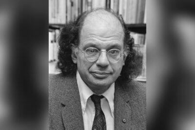 Allen Ginsberg in 1979, in glasses and tweed jacket in front of bookshelves