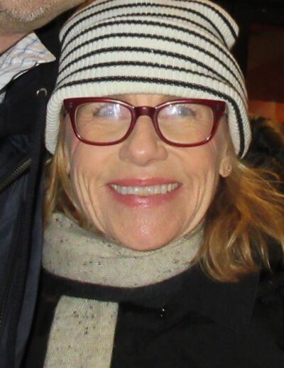 Amy Madigan in a striped knit hat and red glasses, smiling outdoors in New York