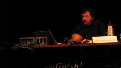 Antoine Schmitt seated at a panel table with a laptop and computer hardware behind his name card at the transmediale.07 festival in Berlin, 2007