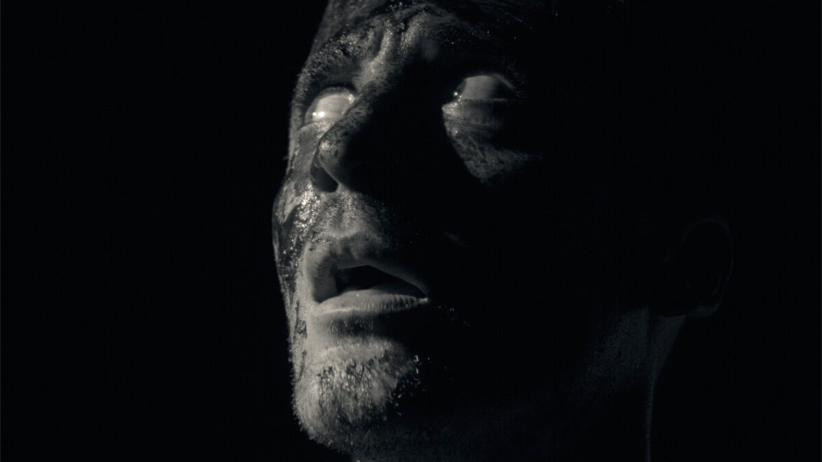 A scarred face emerging from darkness in the black-and-white sci-fi short AURORA