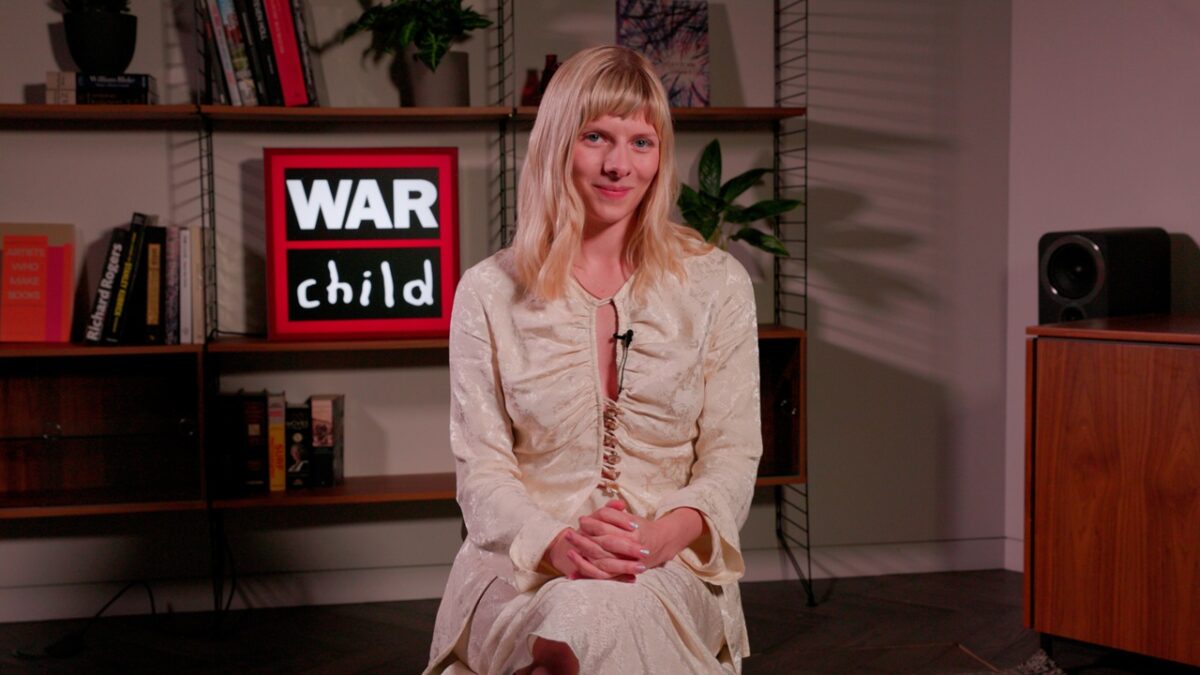 AURORA seated in front of a War Child sign