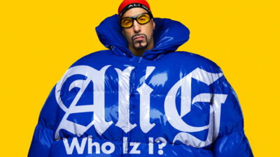 Key art for Sacha Baron Cohen's Ali G: Who Iz I? showing Ali G in an oversized blue puffer jacket on a yellow background