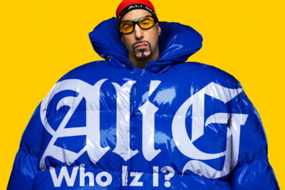 Key art for Sacha Baron Cohen's Ali G: Who Iz I? showing Ali G in an oversized blue puffer jacket on a yellow background