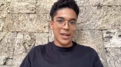 Mexican actor Benny Emmanuel, wearing round wire-rimmed glasses and a black T-shirt, speaks to camera in front of a stone wall in 2021