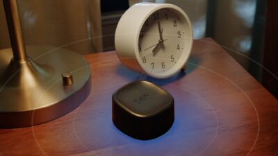 Brick Night app blocker on a bedside table next to an alarm clock, an official product image from Brick