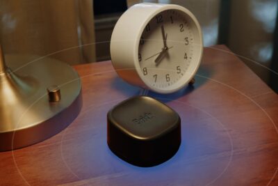 Brick Night app blocker on a bedside table next to an alarm clock, an official product image from Brick