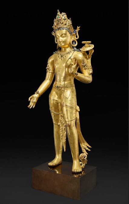 Standing gilt-copper figure of the bodhisattva Manjushri with a jewelled crown and a lotus at his shoulder, on a dark background