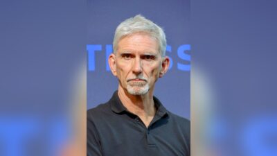 Damon Hill, grey-haired in a black polo shirt, on stage at the Williams Racing Fan Zone at Federation Square, Melbourne, in March 2026