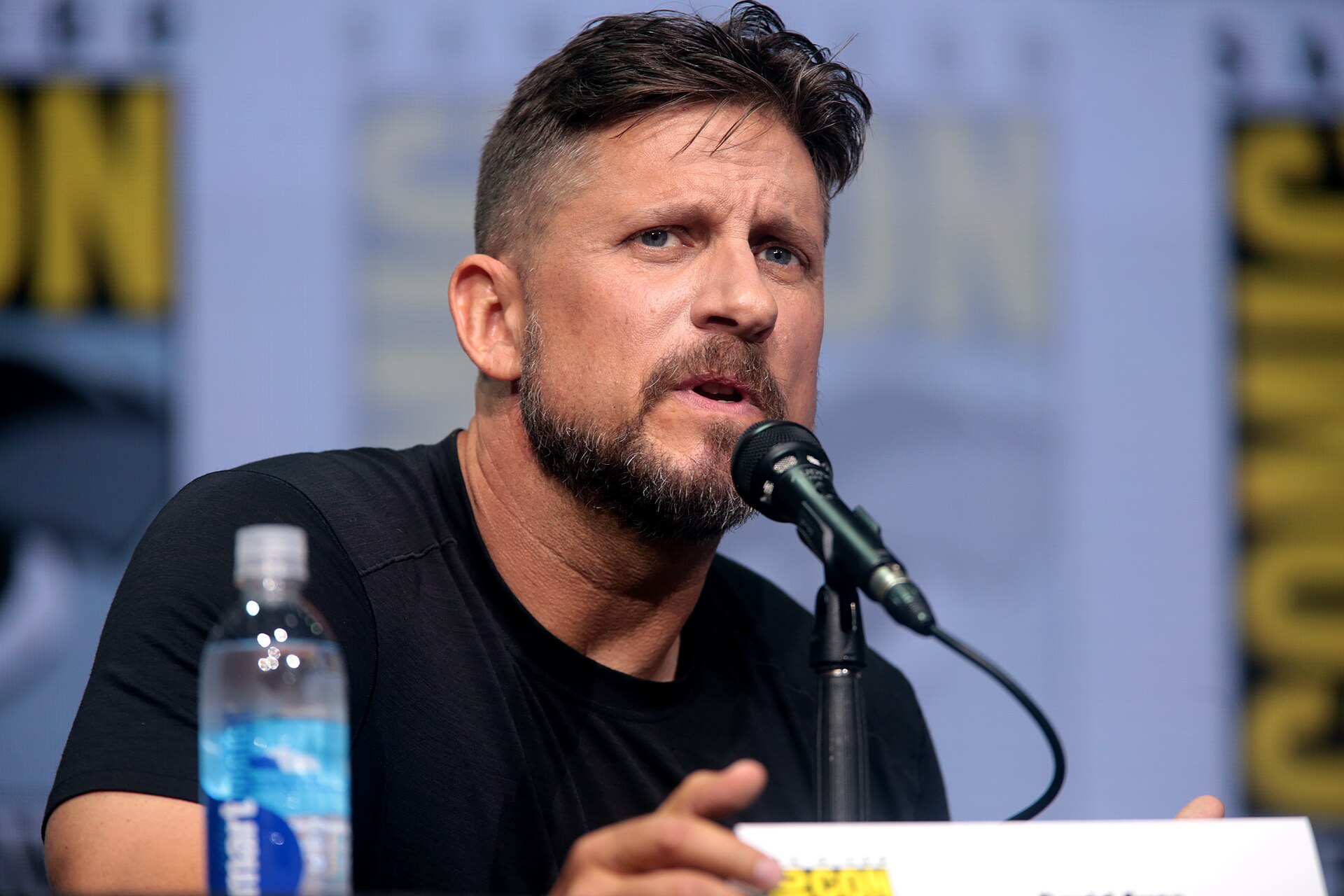 Director David Ayer speaking into a microphone at a San Diego Comic-Con panel in 2017