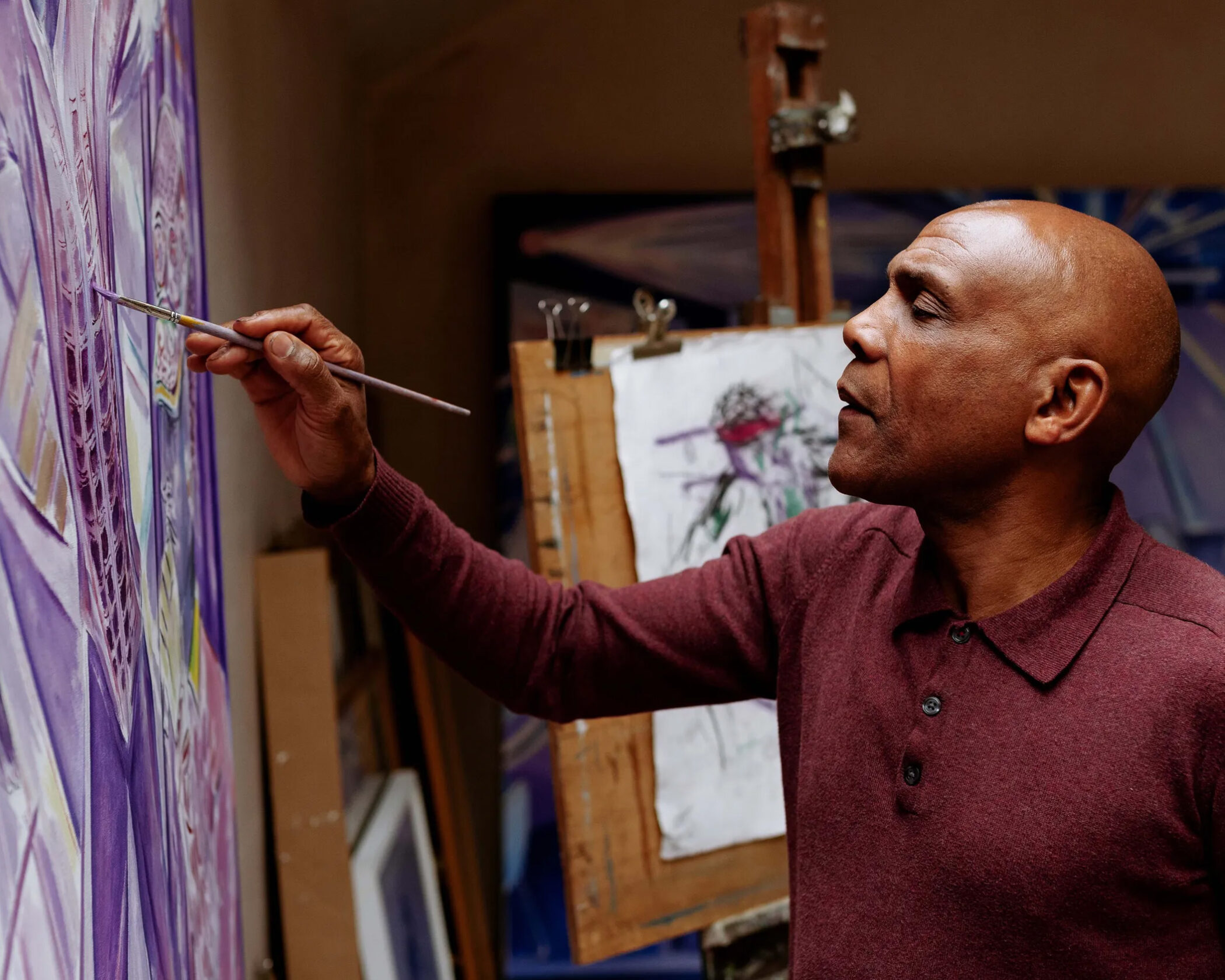 Painter Denzil Forrester working on a large violet canvas in his Truro studio, a drawing clipped to an easel behind him