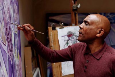 Painter Denzil Forrester working on a large violet canvas in his Truro studio, a drawing clipped to an easel behind him