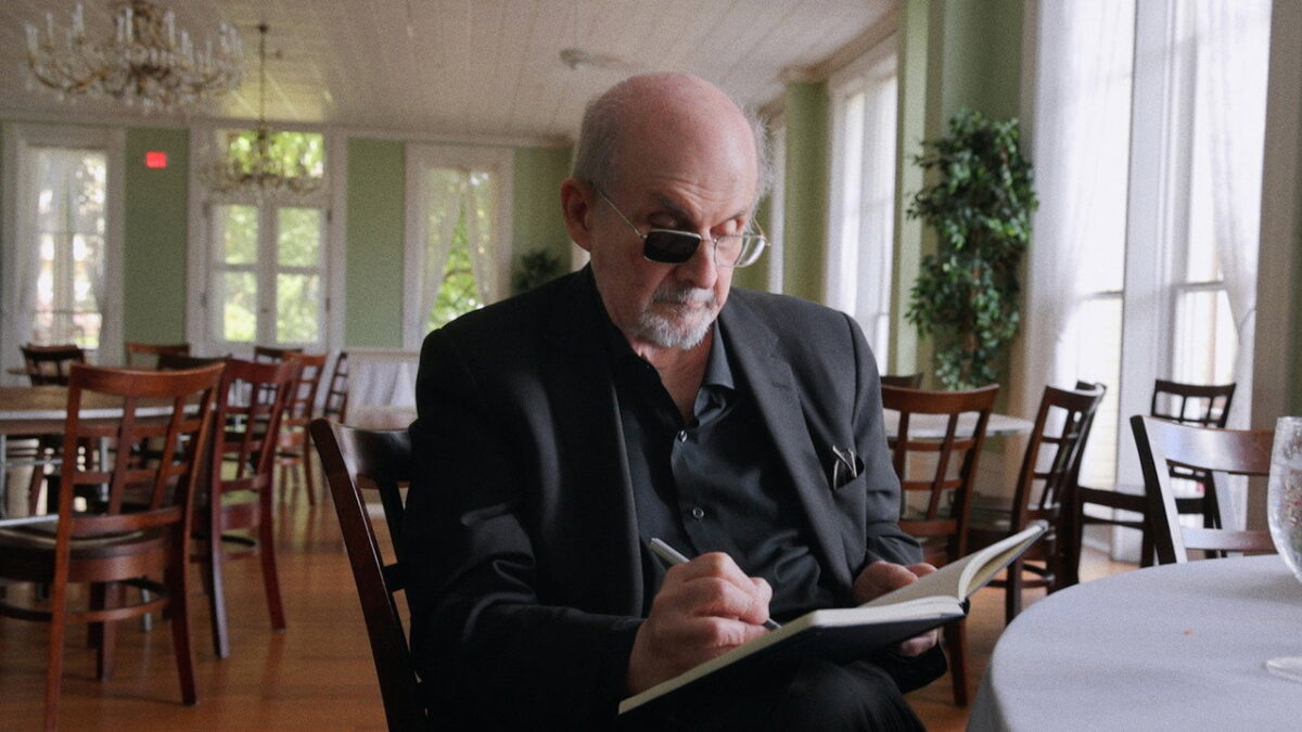 Salman Rushdie writing in a notebook in a still from the 2026 documentary Knife by Alex Gibney