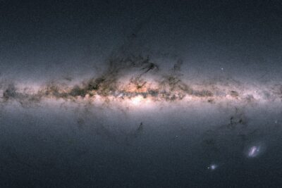 Gaia all-sky map showing the Milky Way as a bright horizontal band of stars crossed by dark dust lanes, with the glowing galactic centre in the middle and two small satellite galaxies below right
