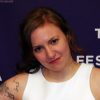 Lena Dunham smiling in a white sleeveless top in front of a Tribeca Film Festival backdrop
