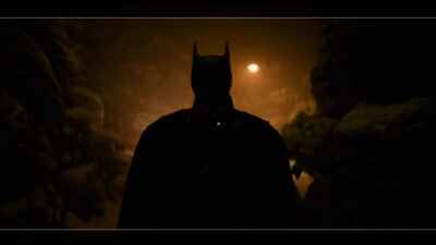 Robert Pattinson's Batman in silhouette against a low orange light in a still from Matt Reeves' Batman films