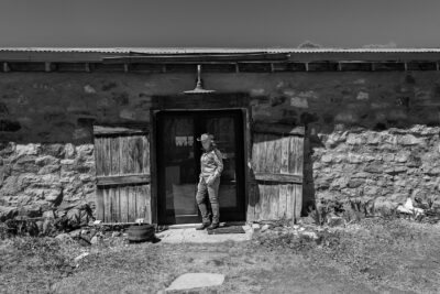 Harmony Hammond in a cowboy hat standing in the doorway of her stone studio in northern New Mexico, black and white photograph