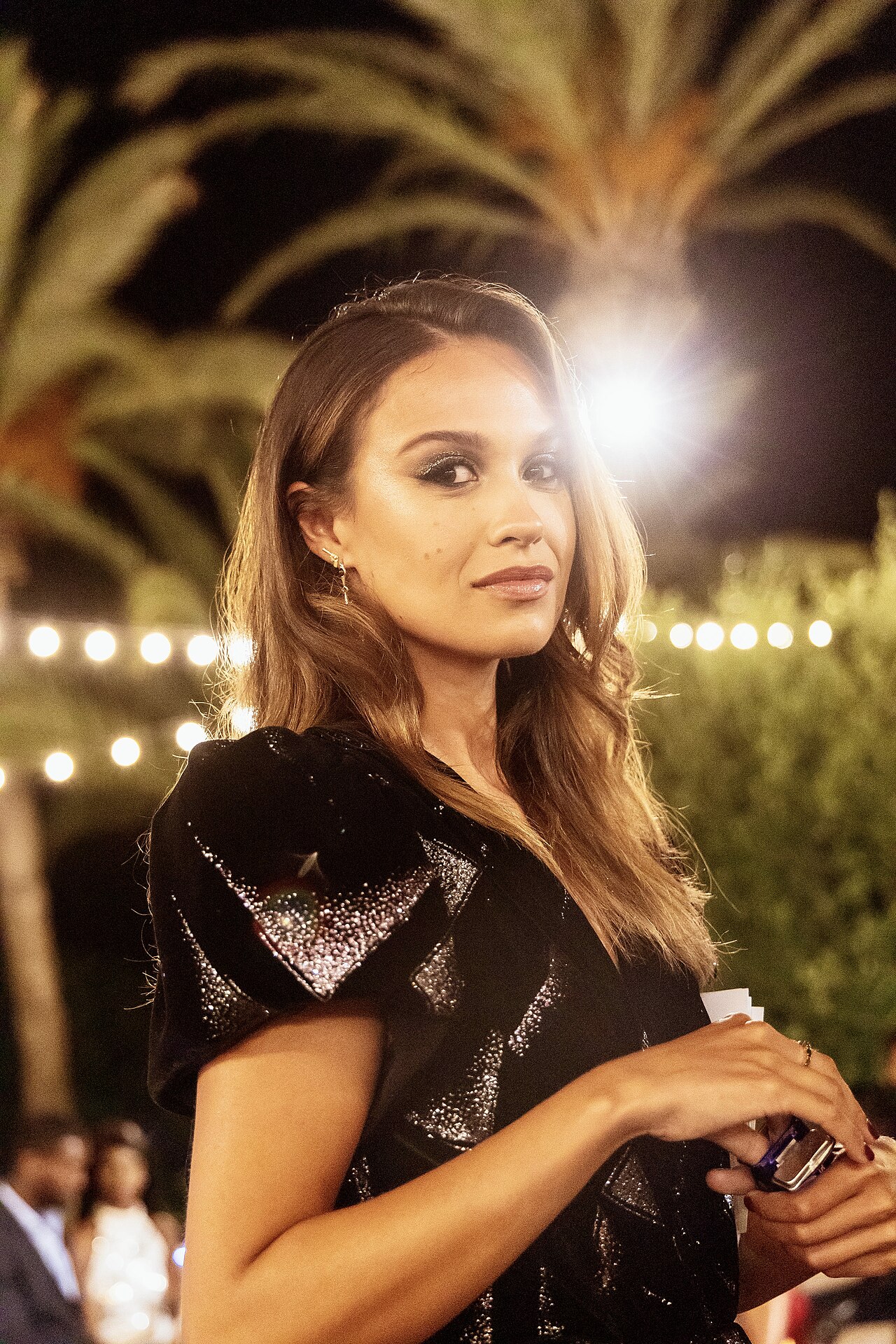 Holly Mae Brood on the set of Love Island at night, in a black sequined dress under palm trees