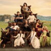 Parker Posey holds a white cat atop a pyramid of leather armchairs seating the cast of The Mob, with Italian vineyards behind them