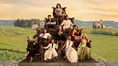 Parker Posey holds a white cat atop a pyramid of leather armchairs seating the cast of The Mob, with Italian vineyards behind them