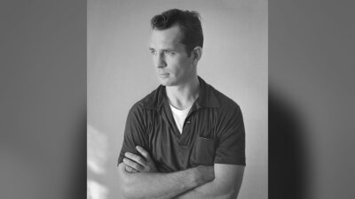 Jack Kerouac photographed by Tom Palumbo around 1956, arms crossed, in a dark short-sleeved shirt
