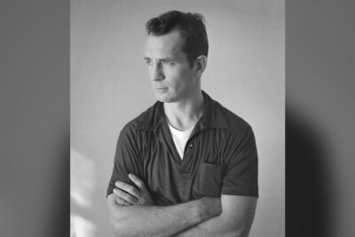 Jack Kerouac photographed by Tom Palumbo around 1956, arms crossed, in a dark short-sleeved shirt
