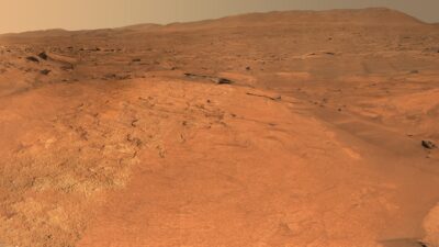 Orange layered bedrock of the Margin Unit on Mars, with the rim of Jezero Crater on the horizon, seen by the Perseverance rover